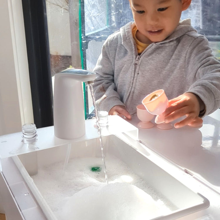 Toddler boy playing with water table with pump and potion stand and test tubes